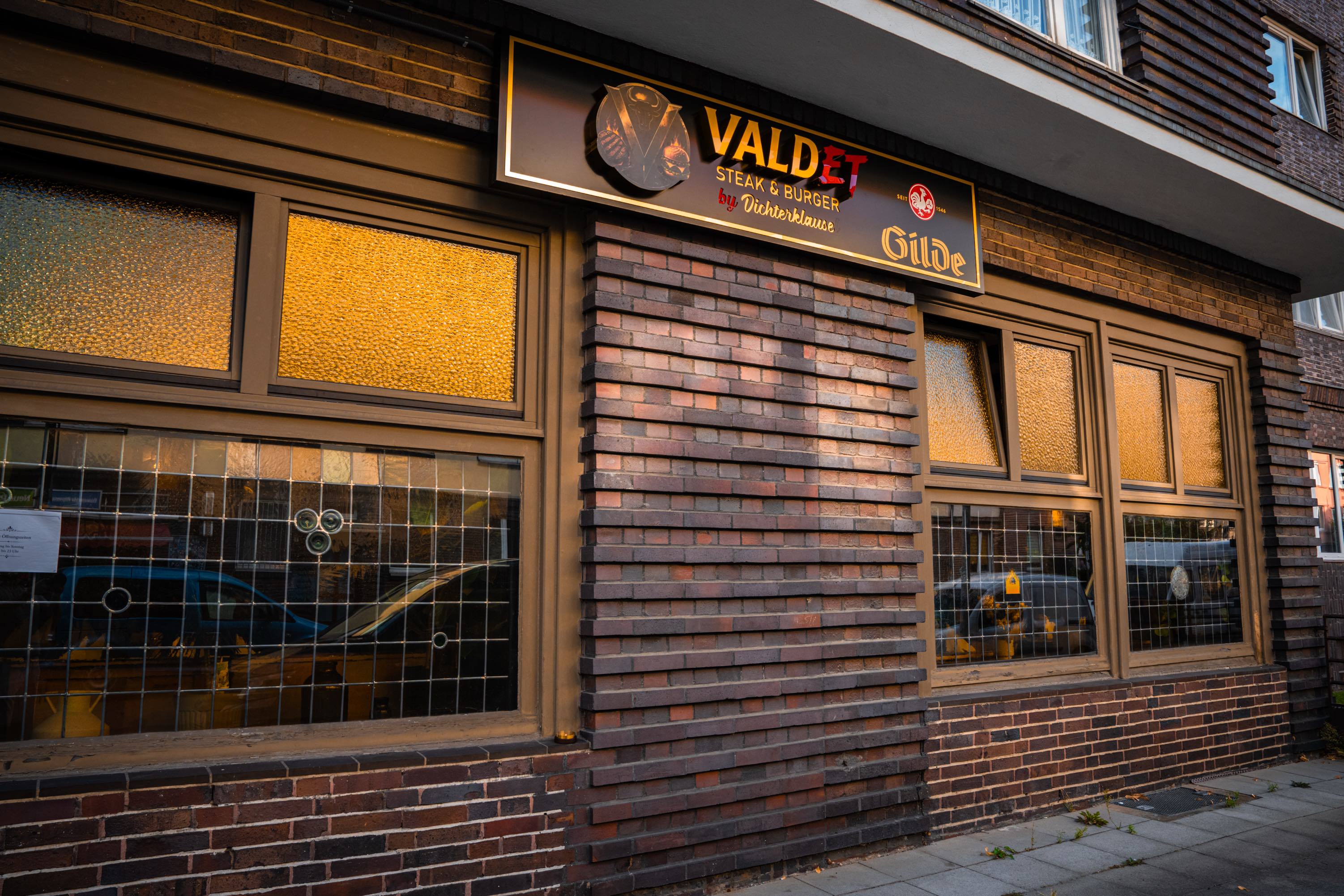 Backsteinfassade mit beleuchtetem VALDET- und Gilde-Schild